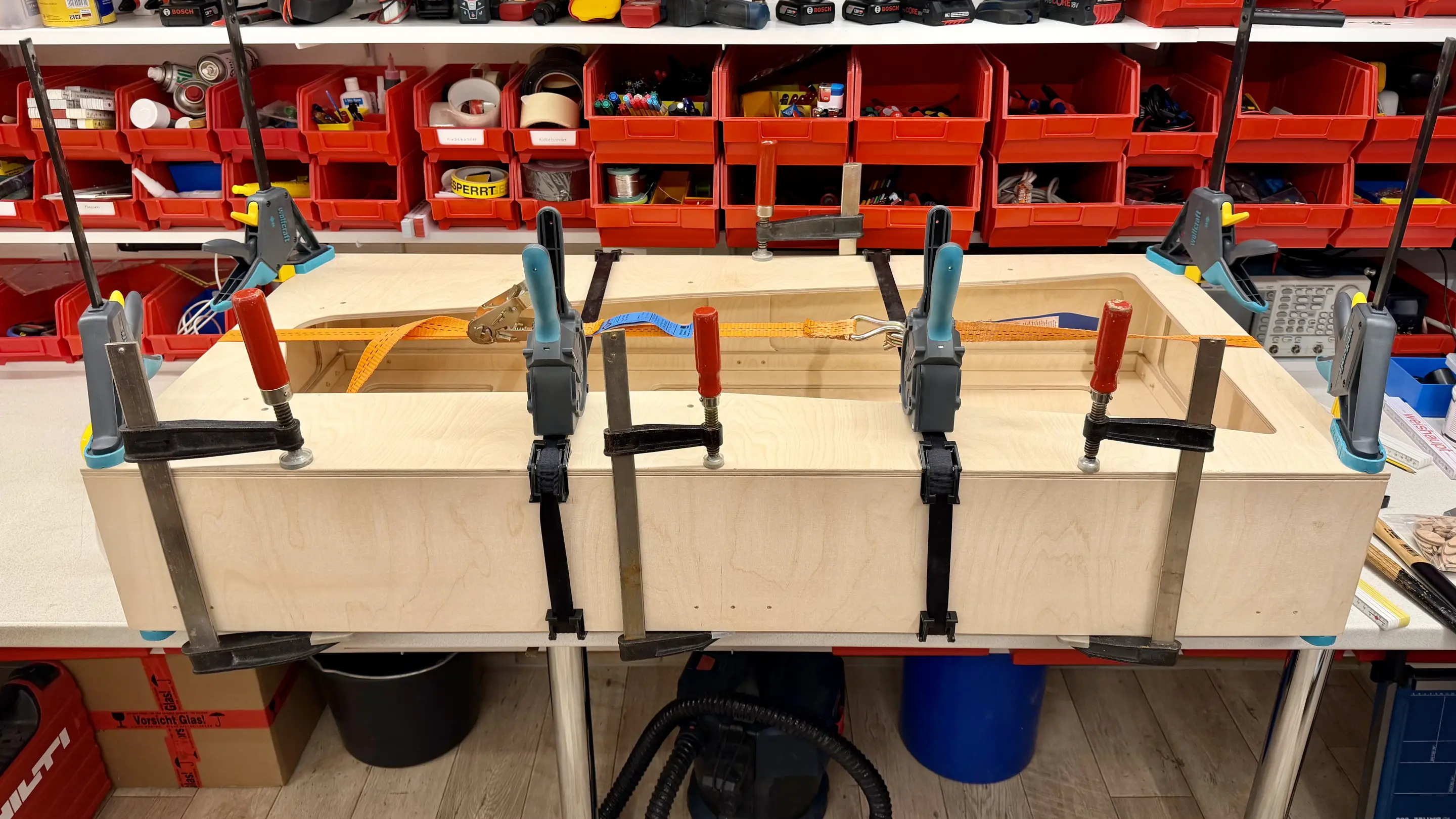 Plywood housing of a trade show exhibit being glued with bar clamps and ratchet straps