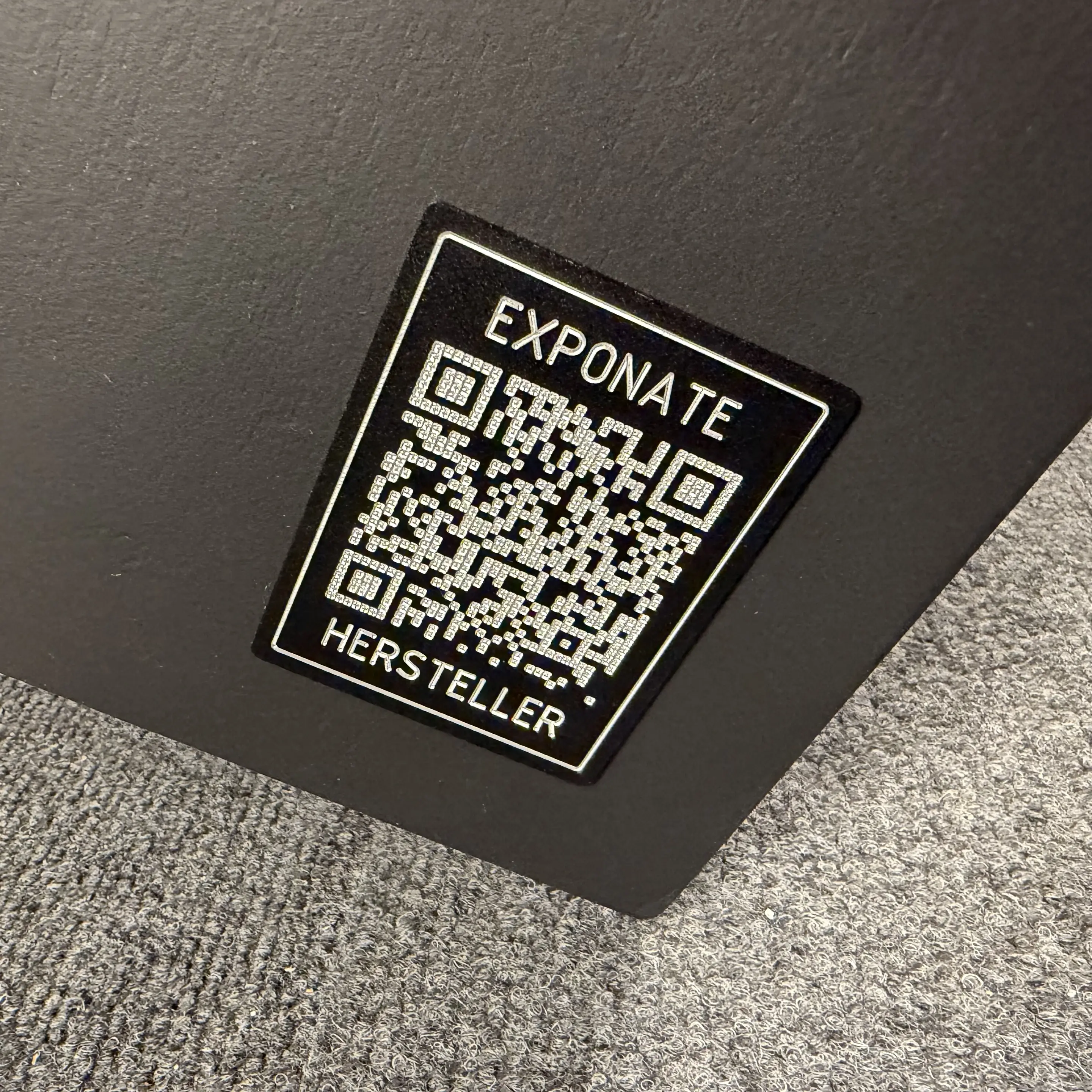 Engraved QR code on black-coated aluminum plate at the trade show exhibit linking to the project page